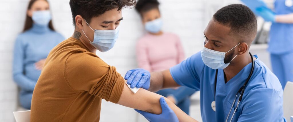A male nurse cleaning a man's arm in order to receive a vaccine. Both men are wearing masks.