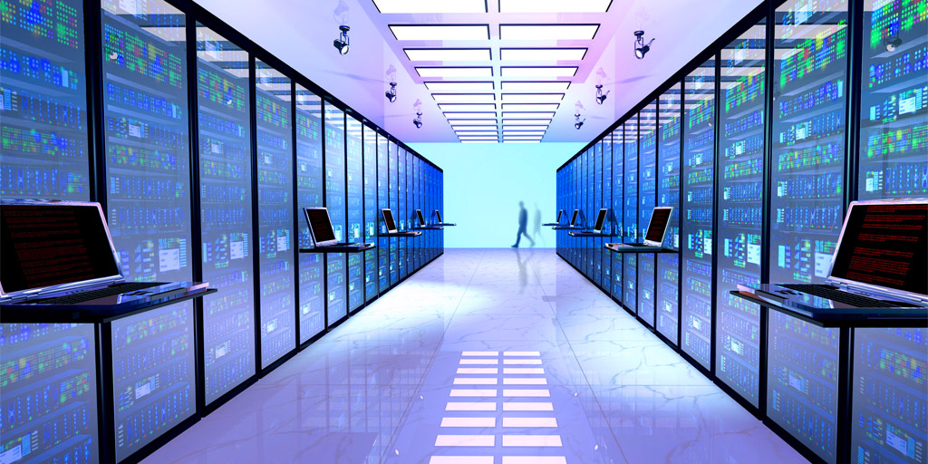 A hallway with laptops lined along each side. Data hardware is located on each side behind glass enclosing.