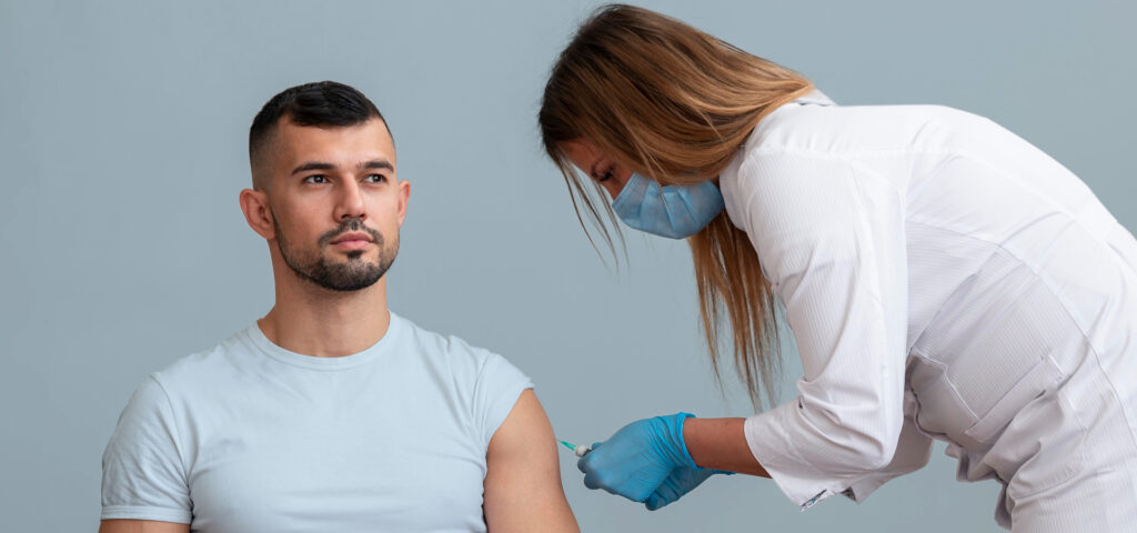 A female nurse is giving a man in a white t-shirt a vaccine.