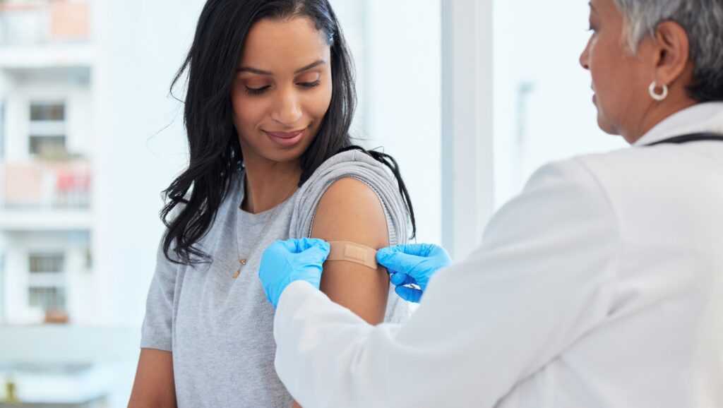 A healthcare professional applies a bandage to a womans arm after administering a vaccine in a clinical setting.