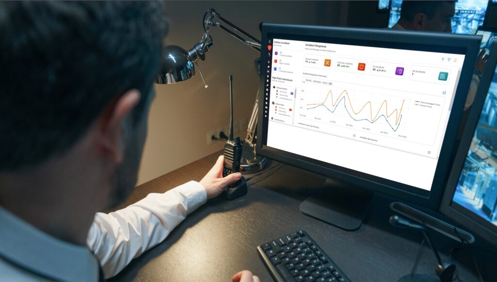 A person at a desk looks at a computer screen displaying analytics graphs, holding a walkie-talkie.