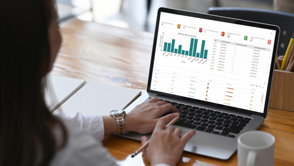 A person using a laptop displaying a dashboard with bar charts and data tables.