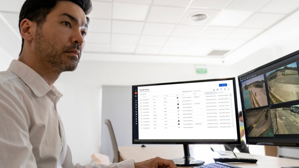 Person at a desk looking at two computer monitors displaying surveillance footage and data.