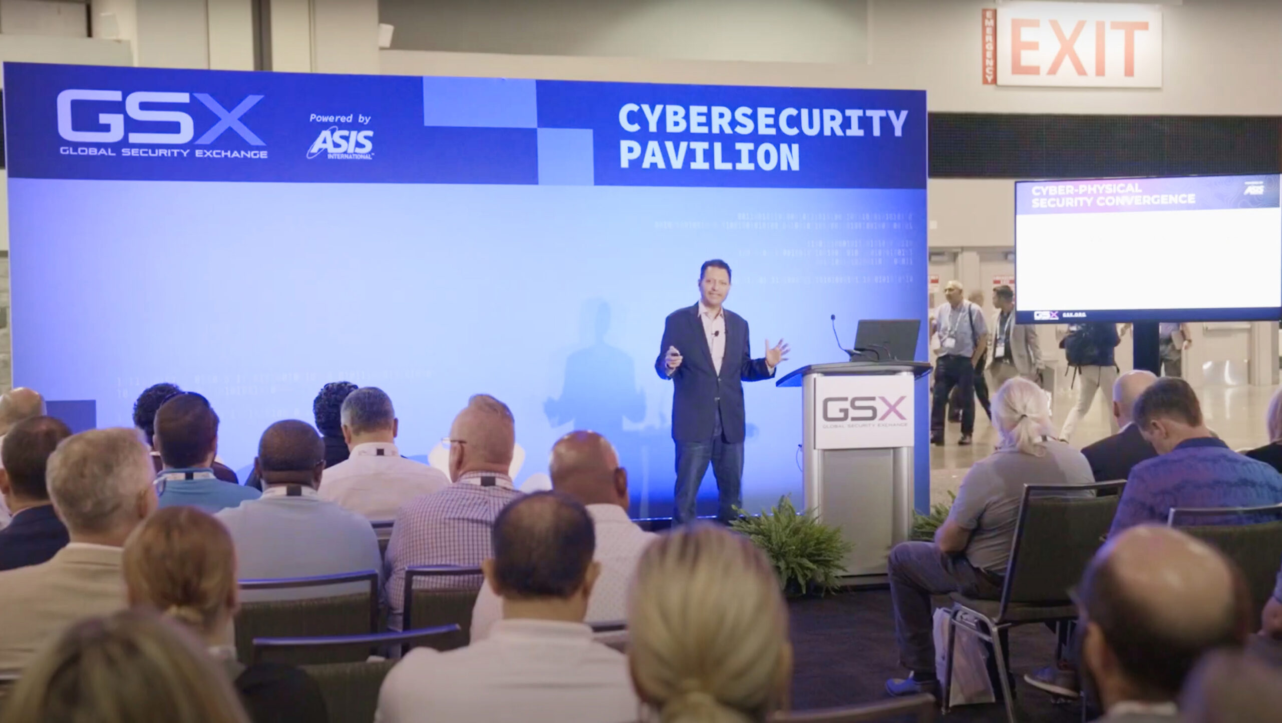 A speaker presents at the Cybersecurity Pavilion during the GSX Global Security Exchange. Attendees are seated and a presentation screen is visible.