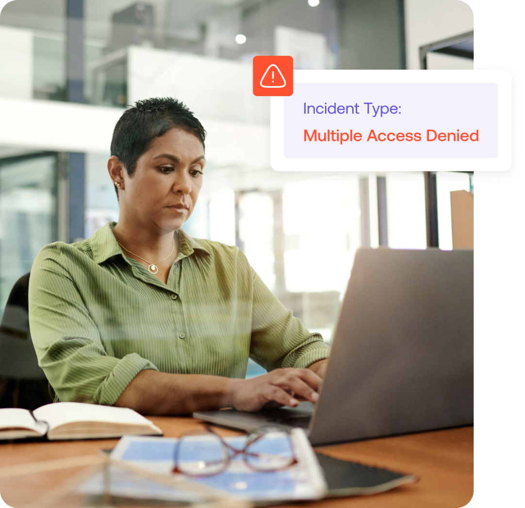 A person in a green shirt works on a laptop in an office. A notification on the screen reads, Incident Type: Multiple Access Denied.