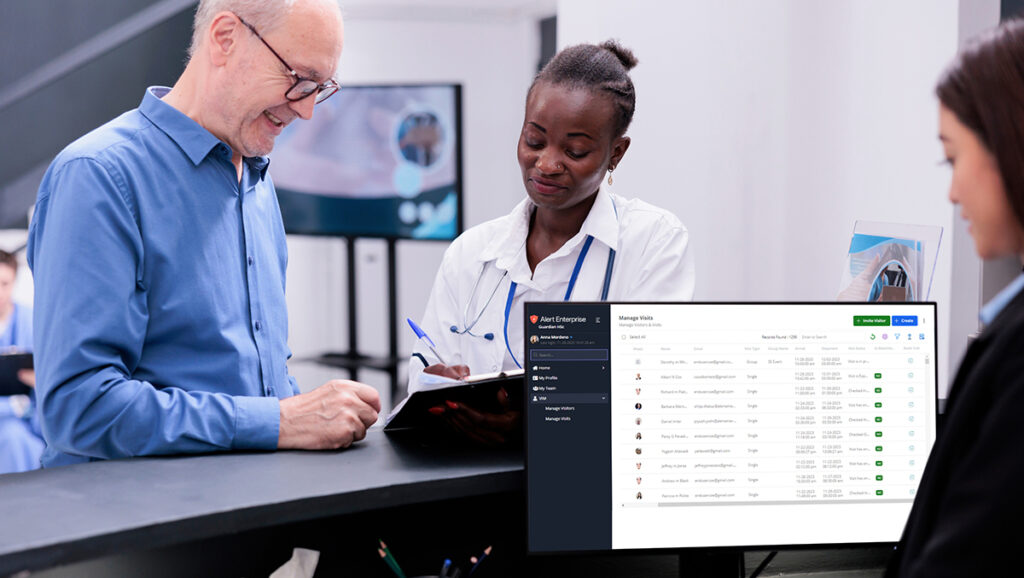 A woman in a white coat assists a man at a counter. A computer screen displays an interface with a list of names and data.