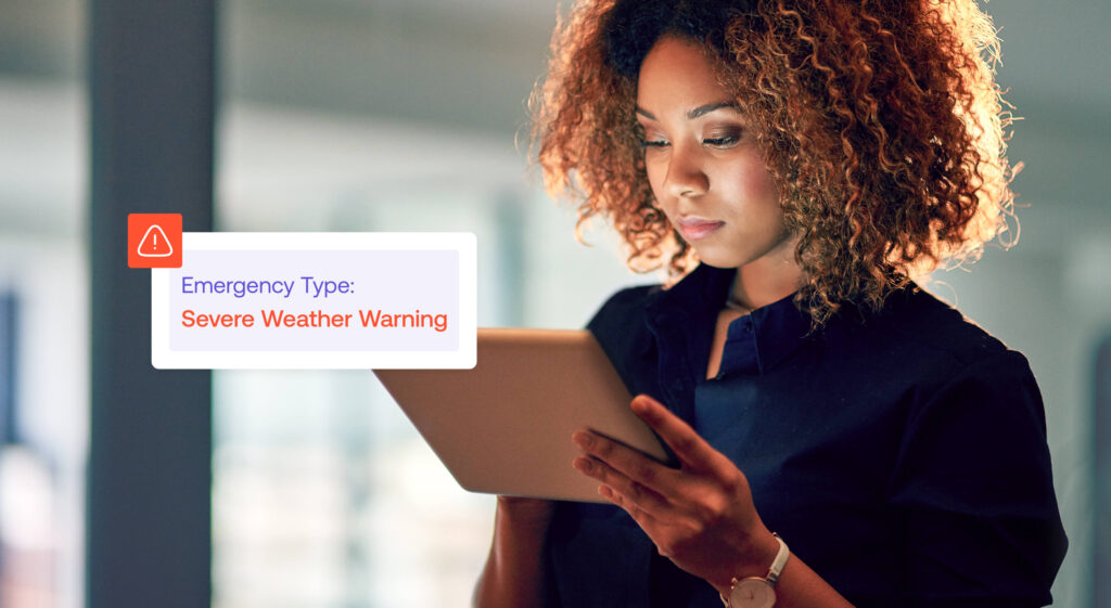 A person looks at a tablet displaying an alert reading, Emergency Type: Severe Weather Warning.