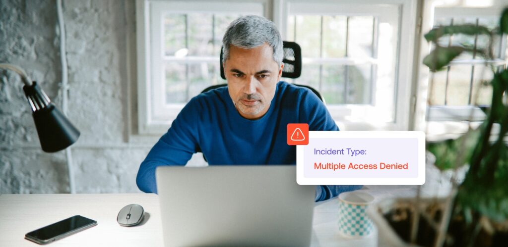 A man sits at a desk using a laptop, with a notification on the screen that reads Incident Type: Multiple Access Denied.