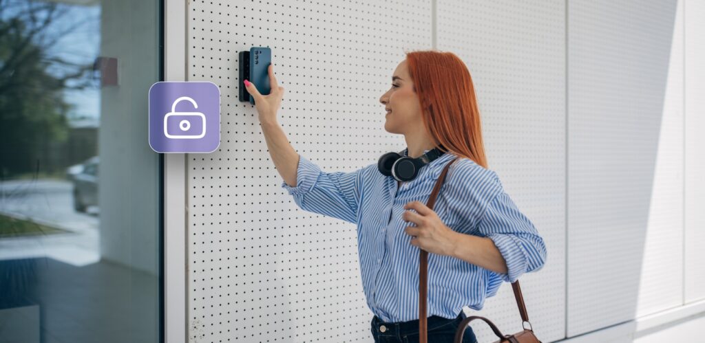 A woman holds her smartphone up to a wall-mounted access control device, unlocking a door as indicated by an open lock icon on the wall.