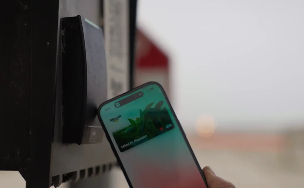 A person holds a smartphone up to a card reader, appearing to make a contactless payment or access using a digital wallet.