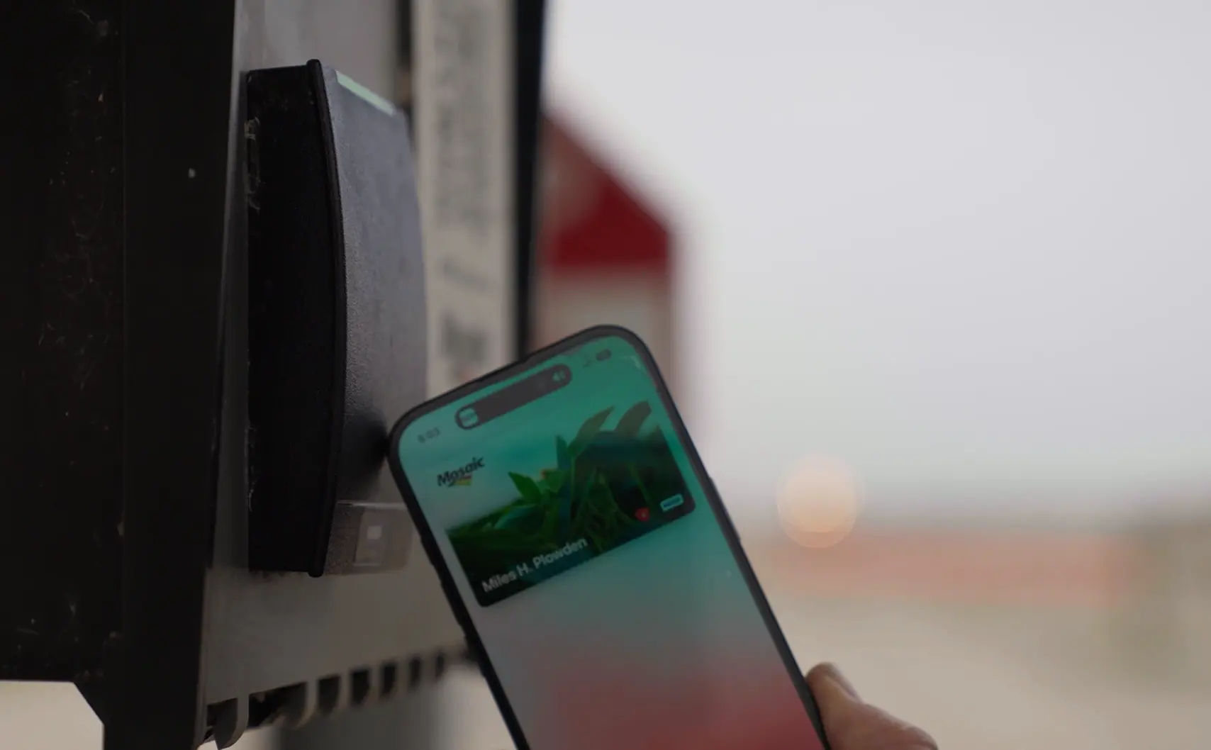 A person holds a smartphone up to a card reader, appearing to make a contactless payment or access using a digital wallet.